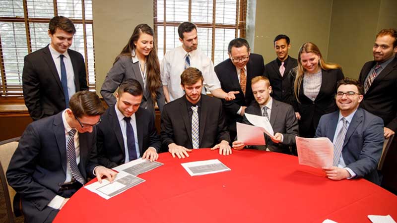 Students sit around red table.